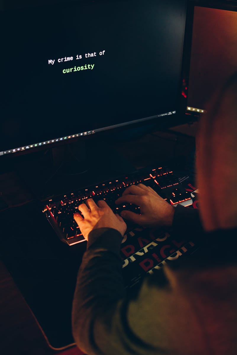 Une personne portant un sweat à capuche tapant sur un clavier avec un écran d'ordinateur affichant un message de curiosité.