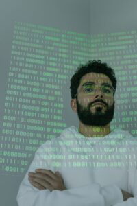 Un homme barbu portant des lunettes se tient debout avec une projection de code binaire, représentant la cybersécurité et l'intelligence numérique.