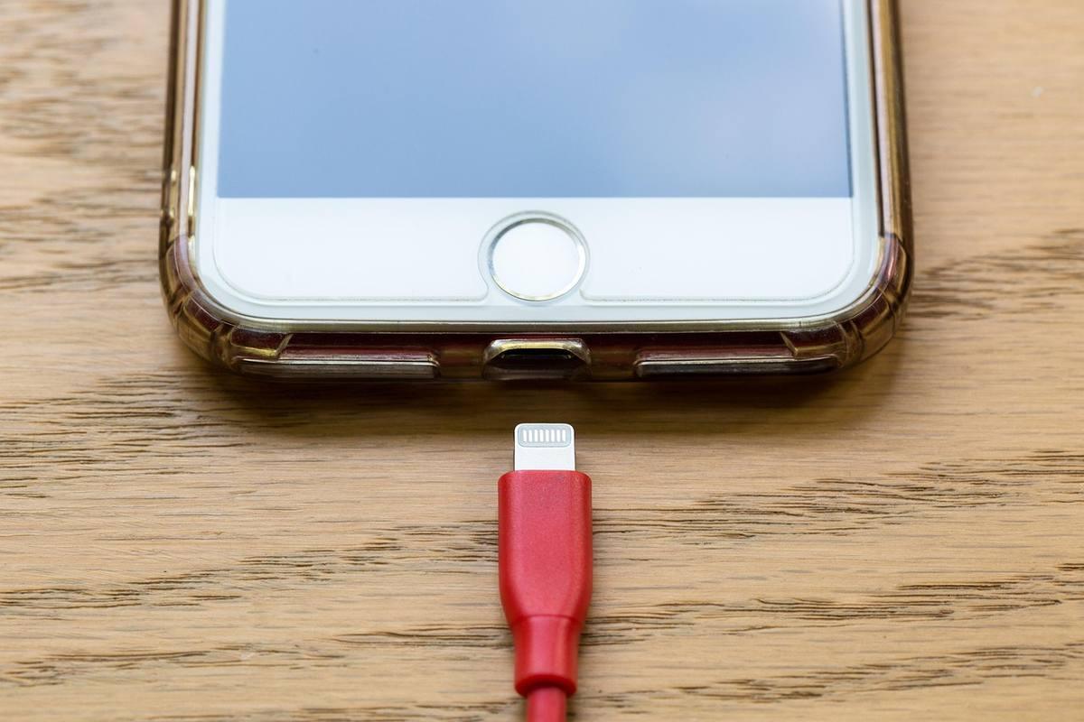 Smartphone connecté à un câble rouge sur une surface en bois Smartphone connecté à un câble rouge sur une surface en bois