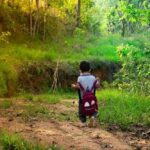 Un petit garçon avec sac à dos marche sur un chemin de terre