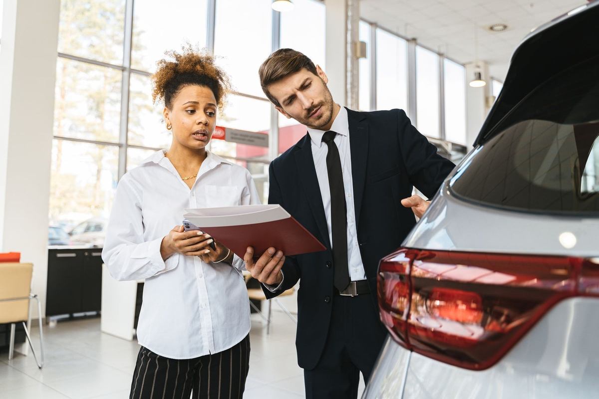 Professionnels discutant d'un dossier devant une voiture dans un showroom Professionnels discutant d'un dossier devant une voiture dans un showroom